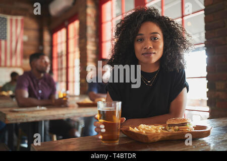 Portrait de femme au Sports Bar manger burger et frites Banque D'Images