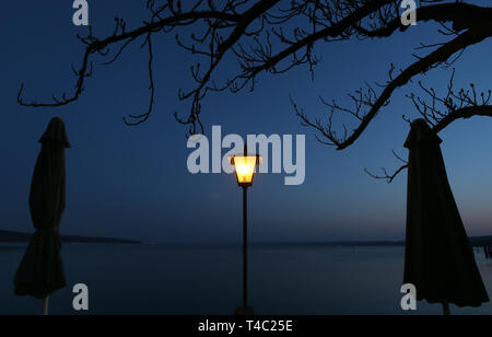Manche, en Allemagne. Apr 15, 2019. Une lanterne est à l'heure bleue dans un jardin au bord de l'Ammersee entre deux parasols. Credit : Karl-Josef Opim/dpa/Alamy Live News Banque D'Images