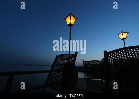 Manche, en Allemagne. Apr 15, 2019. Tables et chaises d'un café en plein air sont à l'heure bleue sur la rive de l'Ammersee en vertu de lanternes. Credit : Karl-Josef Opim/dpa/Alamy Live News Banque D'Images