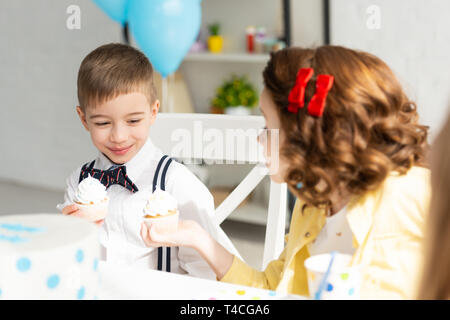 Adorable Kids assis à table et holding cupcakes lors d'anniversaire à la maison Banque D'Images