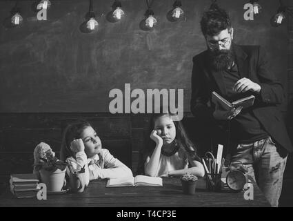 Leçon ennuyeuse concept. Homme à barbe des écolières, enseigne la lecture de livre. L'ennui et les enfants fatigués d'écouter l'enseignant. Enseignant et élèves filles dans Banque D'Images