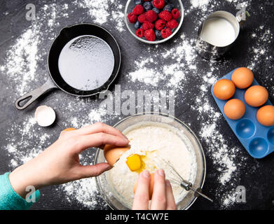 Image de mains d'homme casser des œufs dans un bol. Table avec des petits fruits, du lait, de la farine. Banque D'Images