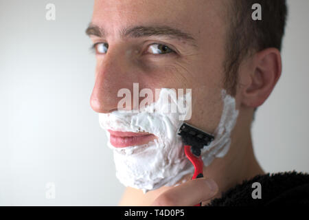 Un jeune homme blanc rasage, face caméra, avec de la mousse sur son visage. Banque D'Images