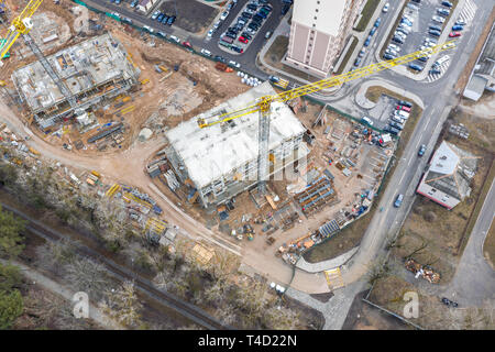 Vue du dessus de l'antenne de la zone de construction de la ville avec des bâtiments inachevés, des grues à tour jaune et des machines industrielles Banque D'Images