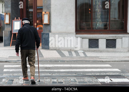 Un homme âgé avec un bâton de marche lentement marche à travers un passage pour piétons au milieu d'une ville seule Banque D'Images