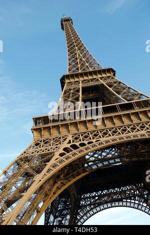 La Tour Eiffel s'étend jusqu'au ciel bleu. Les formes de la structure de métal jaune/marron créer des patterns qu'il jusqu'au-dessus des courbes. Banque D'Images