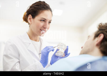 Portrait of female dentist showing patient modèle à dents assis dans fauteuil dentaire, copy space Banque D'Images