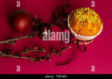 Muffins de pâques décorés avec du ruban et des Sprinkles, les oeufs colorés et une branche d'arbre d'abricot sur un fond rose ou fuchsia. Carte de vœux. Banque D'Images