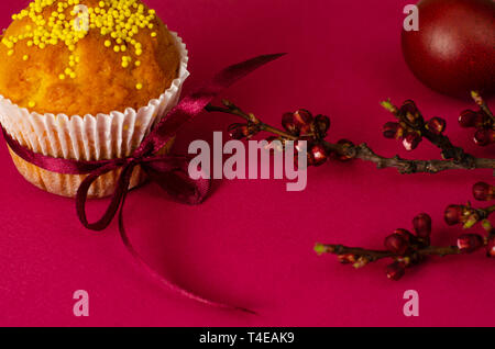 Muffins de pâques décorés avec du ruban et des Sprinkles, les oeufs colorés et une branche d'arbre d'abricot sur un fond rose ou fuchsia. Copier l'espace. Greetin Banque D'Images