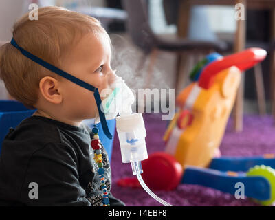 Portrait petit garçon blond avec un masque à oxygène en inhalation à la maison Banque D'Images
