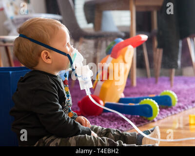 Petit caucasian kid sitting on floor avec masque à oxygène à la maison faire l'inhalation Banque D'Images