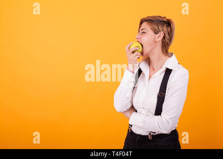 Jolie femme avec les tenues de prendre une bouchée d'une pomme verte sur fond jaune. Belle femme mangeant une pomme verte. Banque D'Images