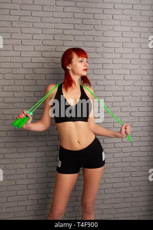 Jeune fille rousse dans les vêtements de sport avec une corde sur un fond de mur de briques gris Banque D'Images