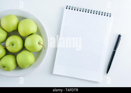 Le concept de l'alimentation. La pomme verte sur une assiette blanche et d'un ordinateur portable avec un stylo. Vue de dessus. Banque D'Images