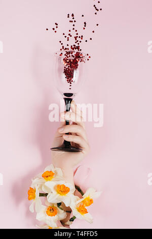 Images créatives de la part des femmes est titulaire d'un verre de vin est perçu à travers un trou dans le papier rose déchiré avec des fleurs et de l'éclaboussure en forme de coeur rouge confettis. Overhe Banque D'Images