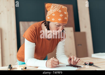 Female carpenter avec foulard tête faisant calcul financier dans l'atelier de menuiserie menuiserie Banque D'Images