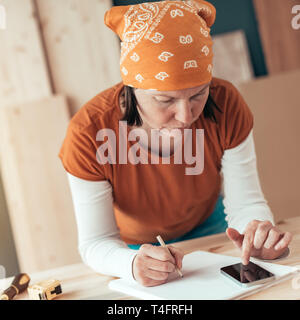 Female carpenter avec foulard tête faisant calcul financier dans l'atelier de menuiserie menuiserie Banque D'Images
