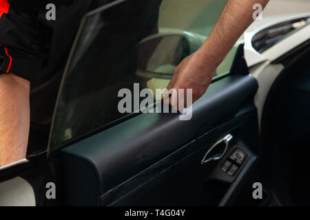 L'assistant d'installation d'équipement supplémentaire bois une teinte film sur le côté de la vitre avant de la voiture et il s'aplatit à la main pour monter la vitre avec un g Banque D'Images