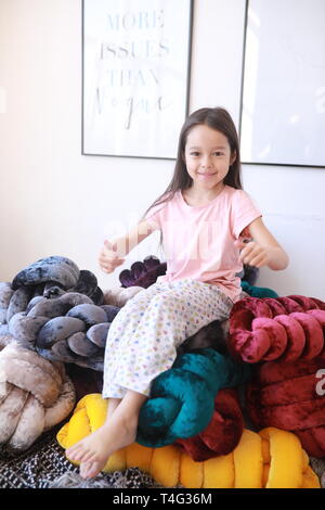 Enfant fille joue sur le lit entre les oreillers multicolore inhabituelle en pyjama. Banque D'Images