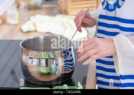 Jeune femme dans la cuisine la cuisine. La soupe est cuite dans une casserole sur la plaque de cuisson Banque D'Images