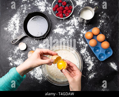 Photo de mains d'homme casser des œufs dans un bol. Table avec des petits fruits, du lait, de la farine. Banque D'Images