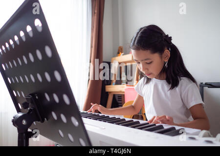 Petite fille asiatique d'apprendre à jouer d'un clavier de piano synthétiseur avec bonheur, Thai girl l'étude de la musique à la maison Banque D'Images