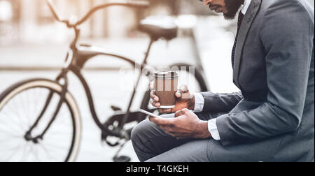 Businessman with coffee et smartphone assis près de bike Banque D'Images