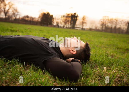 L'homme, sport, se détendre après une formation dans un parc de la ville . Jeune homme sportif relaxant au repos couché sur l'herbe après le long terme et de formation exe Banque D'Images