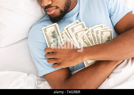 Greedy african american guy dormir et garder un bon nombre de billets de monnaie au lit, vue du dessus Banque D'Images