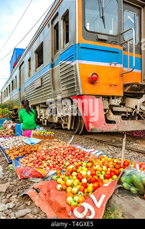 Samutsakorn Province, Thailand - 14 mars 2019 : la vie quotidienne d'un vendeur de rue, la vente de légumes entre les voies ferrées comme dangereusement train passe. Banque D'Images