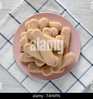 Savoyardi les biscuits sur la plaque en bois blanc, rose sur la surface, vue du dessus. Mise à plat, les frais généraux, d'en haut. Close-up. Banque D'Images