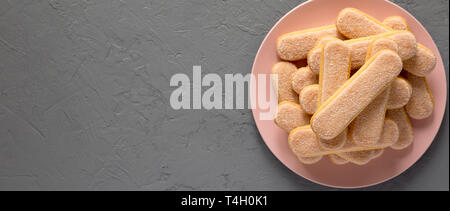 Savoyardi ou biscuits biscuits sur la plaque rose sur fond gris, vue de dessus. Vue d'en haut, d'en haut, une télévision. Copier l'espace. Banque D'Images