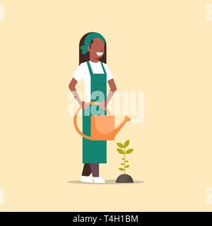 La productrice plantule plante fleur ou légume african american woman holding watering can jardinier dans l'agriculture écologique agricole uniforme Illustration de Vecteur