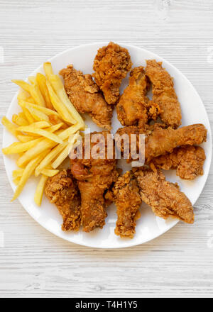 Pilons de poulet frit délicieux, épicé, ailes de poulet frites et les doigts sur la plaque blanche sur la surface en bois blanc, vue du dessus. Mise à plat, les frais généraux, Banque D'Images