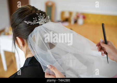 Instituts travaillant sur une femme, les cheveux noirs de la définition d'un voile de tulle dans une coiffure sophistiquée à l'aide de bobby pins et un peigne fin Banque D'Images