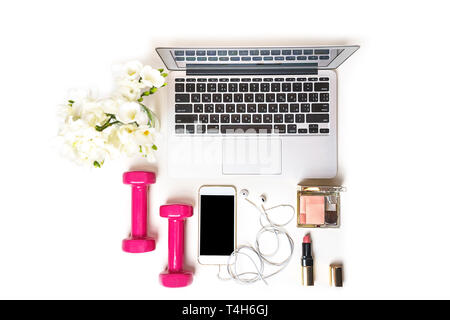 L'espace de travail des femmes avec l'ordinateur portable ordinateur portable, du matériel de fitness haltères rose, miroir cosmétique, téléphone mobile, de casques et de fleur blanche sur fond blanc. Banque D'Images