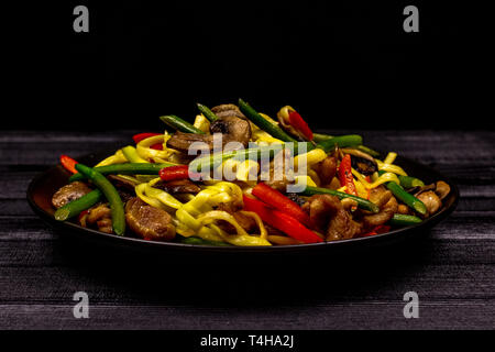 Nouilles sautées appétissant avec de l'ail les germes, champignons, poivron rouge et la viande de poulet sur un arrière-plan d'une rustique noir table en bois. Une populaire Banque D'Images