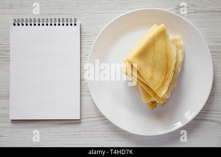 Pile de délicieux blinis sur une assiette blanche, blank notepad over white background, vue du dessus. Mise à plat, les frais généraux, d'en haut. Banque D'Images