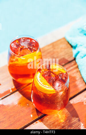 Deux verres d'Aperol spritz et negroni cocktail glacé sur le bord en bois de la piscine avec serviette turquoise. Locations de concept. Banque D'Images