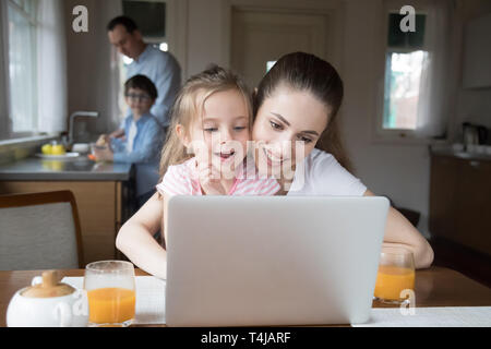 Mère et fille à l'ordinateur pendant que le père et le fils la cuisson Banque D'Images