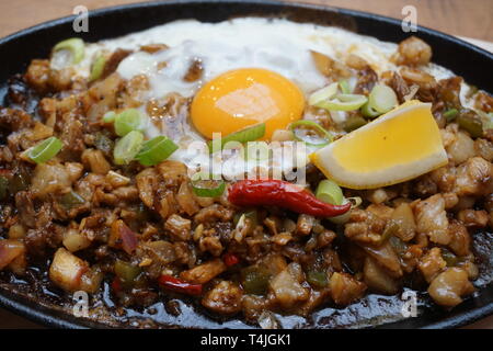 Porc délicieux grésillantes sisig nourriture philippine de porc haché avec l'oeuf cru chaud cuisson sur bac pot en argile avec tranche de citron frais et piments rouges cuisine Asiatique Banque D'Images