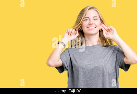 Belle jeune femme portant des T-shirt oversize sur fond isolé Smiling tirant les oreilles avec les doigts, geste drôle. Problème d'Audition Banque D'Images