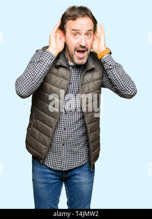 L'âge moyen bel homme portant veste hiver essaie d'écouter les deux mains sur le geste de l'oreille, curieux de ragots. Problème d'audition, sourds Banque D'Images