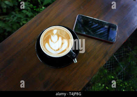 Tasse de café avec de belles Latte art sur bois table de bar à côté d'un téléphone cellulaire Banque D'Images