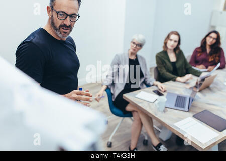 Businessman giving présentation sur tableau blanc à ses collègues dans la salle de conférence. Entrepreneur qui fait sa présentation dans une salle de réunion. Banque D'Images