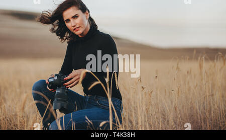 Femme photographe avec appareil photo accroupi dans un champ d'herbe sèche. Femme photographie de paysage en plein air. Banque D'Images