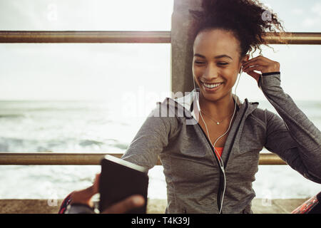 Femme assise à l'athlète, la promenade et l'écoute de la musique à partir de son téléphone. Runner se reposer et écouter de la musique pendant l'entraînement. Banque D'Images