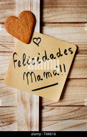 Libre d'un morceau de papier avec le texte felicidades mama, bravo maman écrit en espagnol et d'un cookie en forme de cœur, sur un fond de bois rustique Banque D'Images