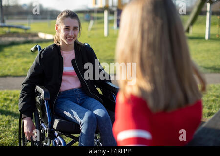 Teenage Girl In Wheelchair Talking With Friend In Park Banque D'Images