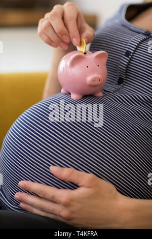 Close Up of pregnant woman Putting coins en tirelire en équilibre sur son estomac Banque D'Images